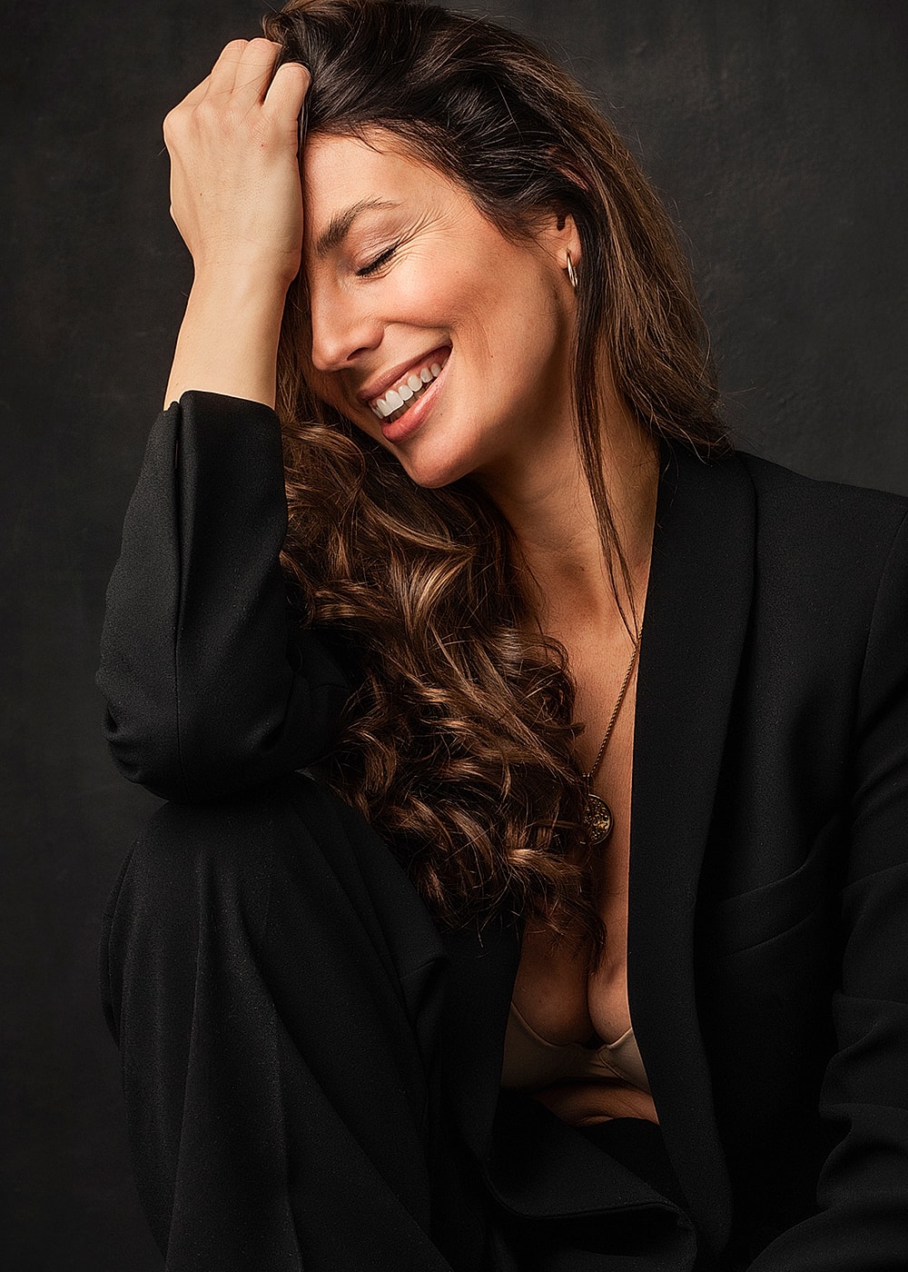 Woman in black suit smiling joyfully.